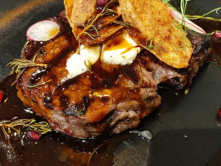 Grilled steak on a dark plate with crispy potato, rosemary, pomegranate and dark jus
