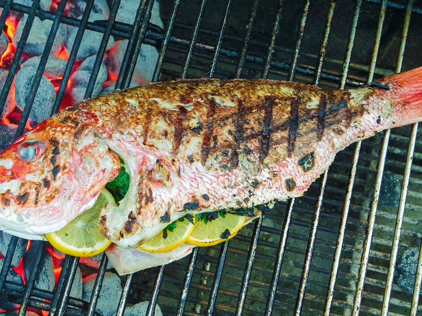 Whole red snapper stuffed with lemon and herbs grilling over charcoal